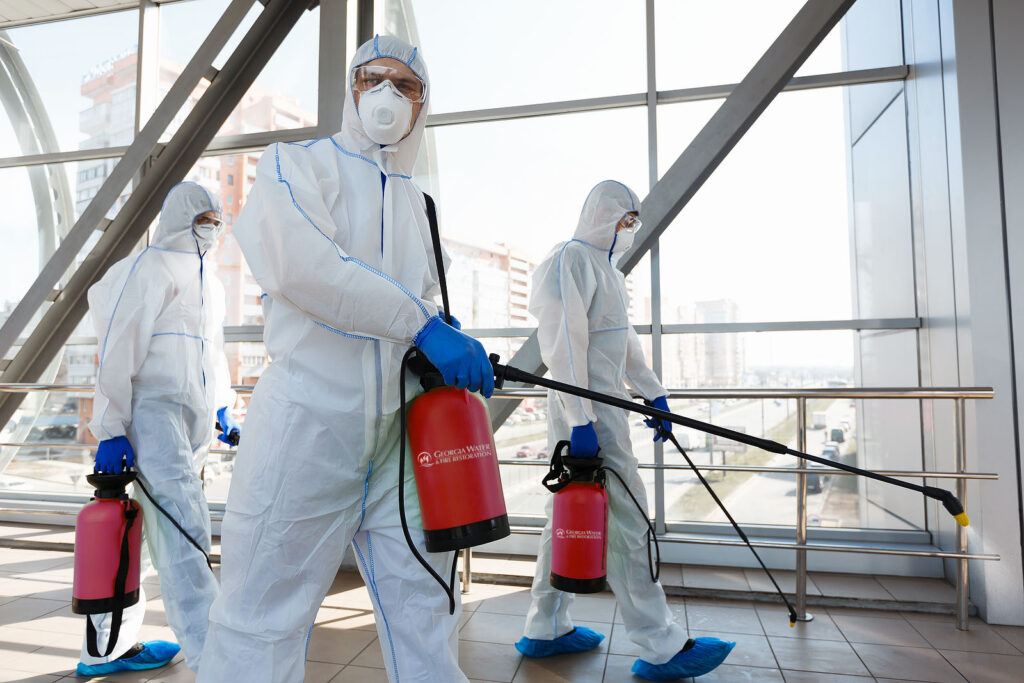 Professional workers in hazmat suits disinfecting indoor accommodation, pandemic health risk, coronavirus